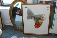 Round ornate mirror and framed lithograph leaning against wall