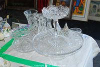 Wide view of crystal collection items including cake plate, candy dish, candle holders, vases arranged on a light cloth.