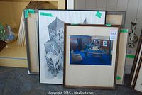 View of three framed pictures leaning against wall: framed signed print by Peter Scott, architectural drawing, and photograph of office interior.