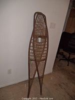 Pair of large wooden snowshoes standing upright against a white wall on a hardwood floor.