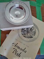 Photo of sterling silver Armada dish on a box with part of the historical booklet visible.