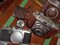Overall view of Leica camera, Zeiss Ikon camera, viewfinder and cases on table