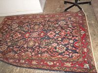 Full view of rug showing navy blue field with multicolored floral geometric motifs and red border