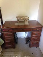 Front view of the vintage wooden sewing desk with 8 drawers and beige Singer sewing machine built into the top