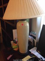 White ceramic table lamp showing tall, smooth vase-like base in white glaze with beige pleated lampshade.