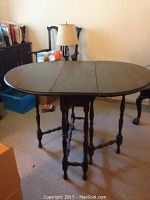 Wooden oval drop-leaf table with swing legs shown fully extended in a room with other furniture items.