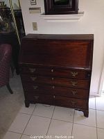 Front view of the wooden secretary desk showing the closed drop-front panel and four large drawers with brass hardware.