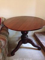 Photo of the entire round wooden pedestal end table showing the top surface and one side with the sofa beside it.