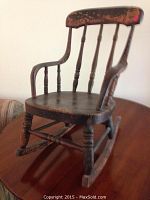 Front and side view of antique child's wooden rocking chair, showing overall shape and wear.