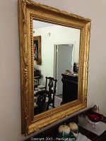 Full view of large rectangular gilded gold wall mirror showing reflection of room interior.