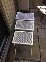 Set of three white wrought iron nesting tables stacked together, showing the mesh tops and metal legs.