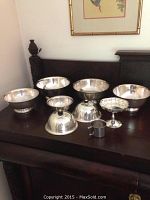Full view of all Revere style bowls, pedestal dish, lids and stainless cup arranged on furniture surface.