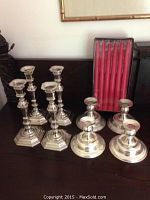 Two sets of silver candlesticks and a box of 12 red candles displayed on a dark wood surface.