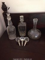 Three cut glass decanters of different shapes with three separate stoppers placed on a dark wooden surface.