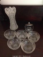 Photo showing entire set: tall vase, small covered dish with metal lid, and five cut glass bowls all with geometric patterns.