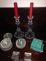 Two clear crystal candleholders each holding a red candle, surrounded by numerous clear crystal drip catchers and a metal snuffer with a green box.