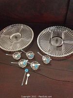 Two round cut glass partitioned servers on a dark background with five small cut glass salt dishes and matching spoons arranged in front of them.
