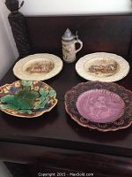 Four decorative plates and one ceramic stein displayed on a dark surface.