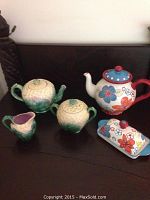 Set of five ceramic items: two cabbage-themed teapots, creamer, sugar bowl, floral-themed teapot, and floral butter dish arranged on a dark surface.