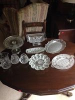 Full set of clear cut glass serving ware displayed on a wooden table, showing each piece distinctly including cake stand, pitcher, goblets, and various serving trays.