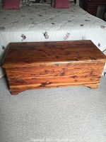 Front and top view of the rectangular cedar chest with natural finish, placed in front of a bed.