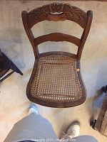 Front view of wooden chair showing carved floral motif on backrest and woven rattan seat.