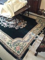 Photo showing the dark green and cream-beige floral patterned carpet with part of a wooden table on top.