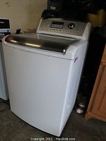 Front three-quarter view of white top-loading washing machine in storage area