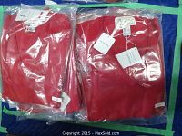 Two red men's sweaters in sealed plastic packaging with tags visible, lying side by side on a blue surface.