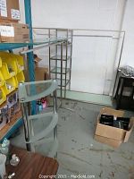Photo showing the stainless steel garment rack with overhead clothing rod and glass base shelf in a storage area.