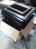 Stack of black velvet jewelry display frames with gold trim inside an open cardboard box