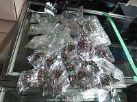 Overview of assorted new bracelets and necklaces individually packaged in plastic bags on glass surface.