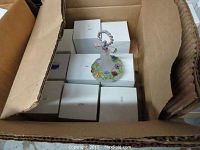 Box filled with multiple white boxed perfume bottles and one displayed on top, showing floral designs and frosted glass.