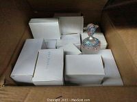 Box of white-packaged perfume bottles with one decorative bottle on top.