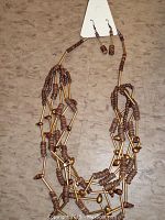 Photo showing multi-strand necklace with brown wooden beads and brass-colored metal tubes laid on a surface.