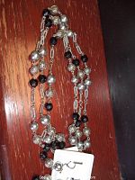 Silver-tone, filigree, and black bead necklace laid on wood surface showing bead details and chain.