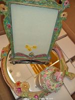 Photo showing one floral perfume bottle and one floral picture frame on a mirror tray with floral design.