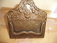 Close-up image of a decorative metal card holder featuring raised floral and scrolling details, showcasing vintage style and patina.