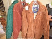 Three men's coats hanging on hangers: one solid green coat and two tan suede coats with patterned lining.