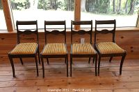 Four wooden chairs lined up against a window, view from the back showing the dark wooden frames and striped upholstery.