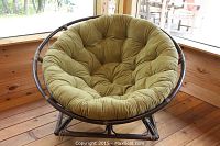 Front view of the large round Papasan rocker showing olive green tufted cushion and dark brown rattan frame on wooden floor.