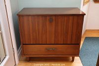 Front view of the wood liquor cabinet showing the closed fold-down front panel and drawer below.