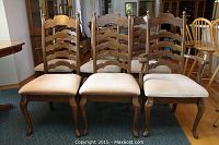Front view of oak ladder-back dining chairs with off-white upholstered seats, three chairs shown in front row