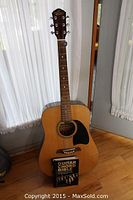 Full view of Oscar Schmidt by Washburn acoustic guitar standing upright with Guitar Chord Bible book resting on guitar body