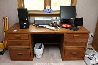Front view of oak desk with computer tower, printer, monitor, speakers, keyboard, mouse, power strip, and tissue box on top.