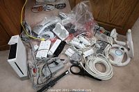 Overview photo showing Nintendo Wii main console, controllers, steering wheels, cables, and other accessories arranged on floor