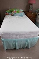 Single bed with King Koil white quilted mattress and matching boxspring with light blue skirt and stacked colorful nature-themed comforter and pillow on top.