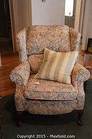 Front view of floral upholstered wing back armchair with a striped pillow on the seat.