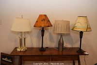 Four table lamps on wooden table, two with hand-painted shades and two with traditional styled shades and bases