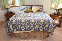 Front view of the queen bed with blue floral bedding, pillows, and sand-colored bed skirt; shows mattress height and bedding.